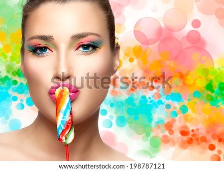 Sweet kiss. Candy girl. Close up portrait of gorgeous young woman with light makeup, looking at the camera with colored sweet candy on her sexy pink lips. Colorful background.