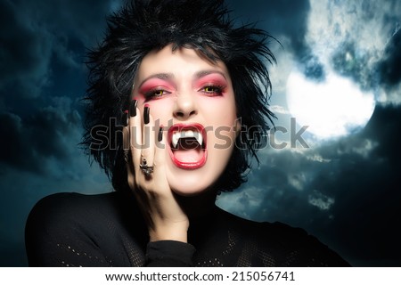 Female werewolf. Beautiful young woman screaming with fangs, wolf lenses and decorated nails. Halloween concept