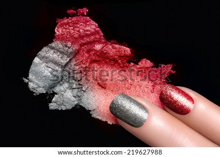 Fingers with trend glitter nails in red and silver. Crushed eye shadow with drops of water. Manicure and makeup concept. Closeup image isolated on black