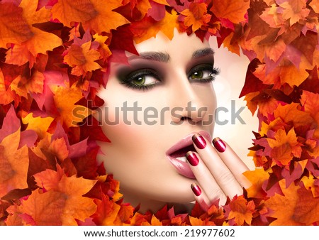Autumn makeup and nail art trend. Fall beauty fashion girl. Professional makeup and manicure. Closeup face fashion model appearing between the leaves