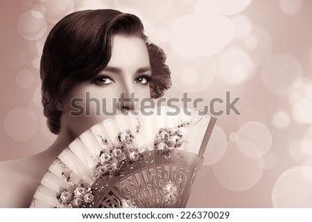 Gypsy girl. Beautiful Andalusian woman with carnation in hair and covering half face with a stylish fan. Spanish beauty. Fine Art portrait in sepia with copy space for text.