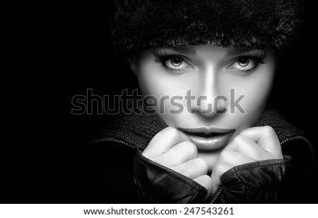 Winter Beauty Fashion. Closeup gorgeous young woman wearing trendy fur hat and mittens. Looking at camera sensually. Monochrome high fashion portrait isolated on black  with copy space. Wintry style