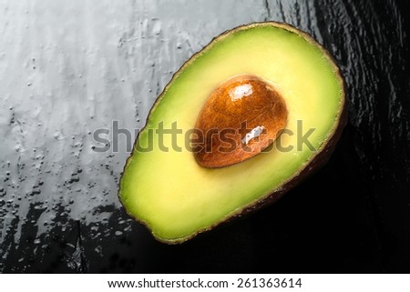 Top view close up of a half ripe avocado on smooth black surface. Clean eating and healthy diet concept