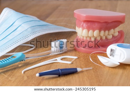 Set of false teeth with dental cleaning tools including a toothbrush, dental floss, disposable face mask and plastic flossing tool in an oral hygiene concept