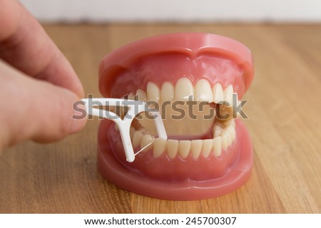 Man cleaning a pair of false teeth with dental floss demonstrating how to clean between the teeth over a wooden background
