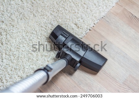 High angle view looking down the handle of a modern vacuum cleaner being used to vacuum a long pile white carpet