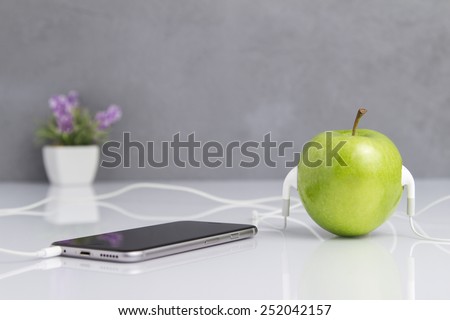 Close up Shot of Conceptual Green Fresh Apple with Headset Connected to Smart Phone on the Table.