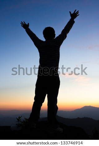 Silhouette of man on a summit with upraised arms  on the top mountain with the sunset, Praise for GOD.
