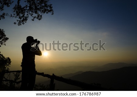 silhouette of a photographer who shoots a sunset in the hill
