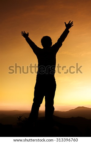 Silhouette of man on a summit with upraised arms on the top mountain with the sunset, Praise for GOD.