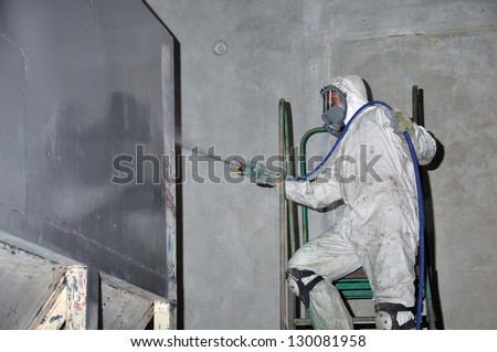 A tradesman uses an airless spray to paint a coal hopper inside a manufacturing plant