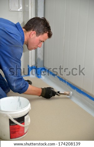 tradesman painting edge of floor line before epoxy product is used in an industrial building