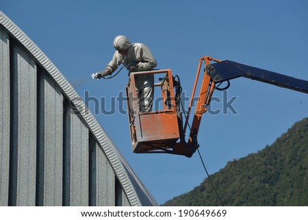 Tradesman spray painting the roof of an industrial building