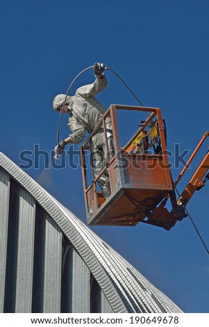 Tradesman spray painting the roof of an industrial building