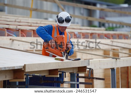 A builder uses a nail gun to secure timber on the verandah of new building