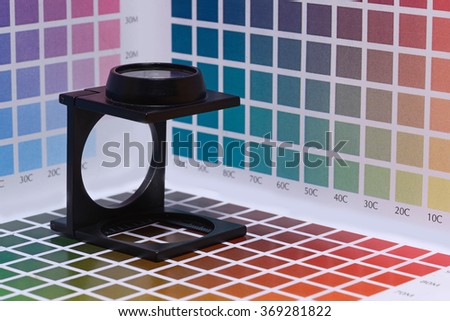 a magnifier or printer\'s loupe sits on a colour test sheet in a pre-press workshop