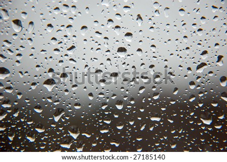 Rain drops on a window glass, with un-sharpen clouds and forest in the background.