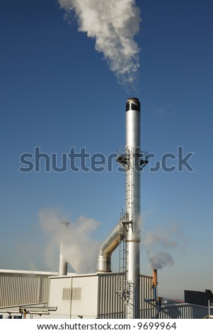 Stainless steel industrial chimney with buildings at the bottom of it.