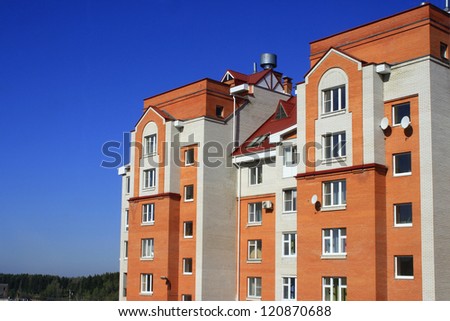 Photo of big brick red-white house being on suburb of city, against blue sky