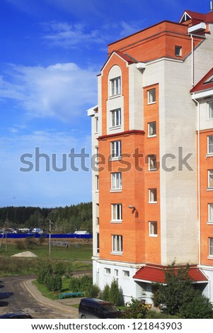 Summer photo of big brick house against blue sky and wood