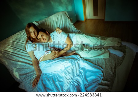 Couple expecting baby. Happy future dad and his cheerful caucasian pregnant wife lying on bed at home and dream of the future.
