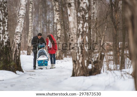 Young family walk in winter wood. Parent pulling sledge through snowy landscape. Woman and man are having walk in countryside in bright sunny day.