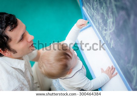 Image of cute little daughter with her young dad. Father and baby girl outdoor. Teacher tells  child on chalkboard