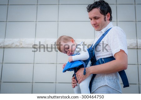 Image of young father and his asleep baby walking in baby carrier in city. Daddy and daughter outdoor.