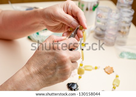 Closeup of pliers and hands assembling a bead necklace.