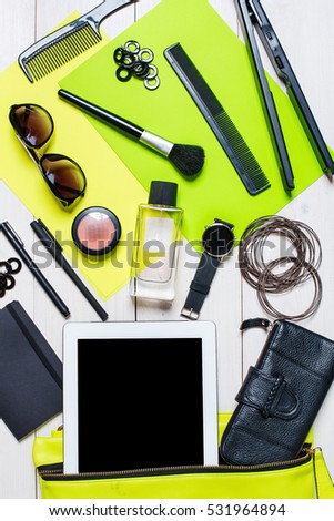 Cosmetics and women\'s accessories fell out of the green handbag on white background.