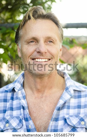 handsome smiling mature blond man with stubble wearing a blue checked shirt.
