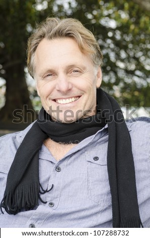 handsome smiling mature blond man wearing a black scarf and blue shirt.