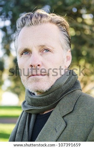 pensive looking mature man with beard wearing a green scarf and jacket.