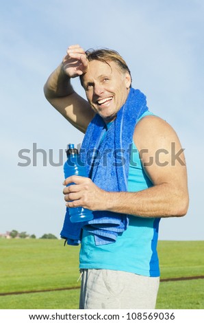 happy smiling sportsman wiping sweat from his head while holding a blue water bottle.
