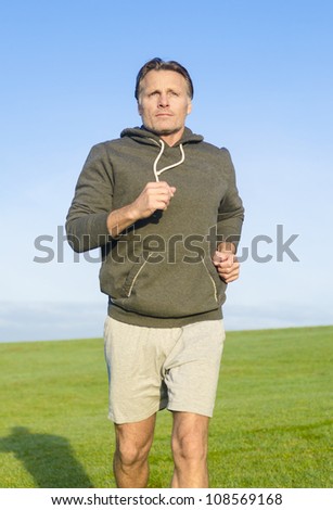 man jogging in park wearing a grey sweatshirt and shorts.