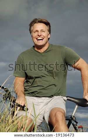 A handsome fit forties man takes a break during a bike ride in the countryside while dark storm clouds roll in behind him.He has a fabulous smile.
