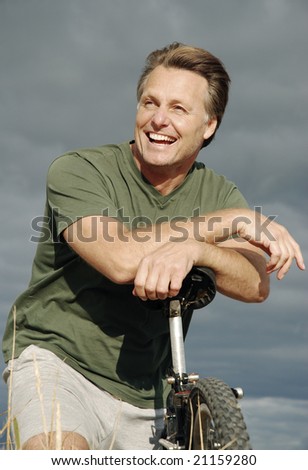 A healthy fit forties man takes a rest on his mountain bike and smiles during a day of cycling at the beach