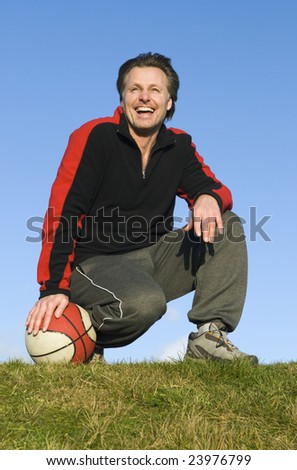 A handsome forties sportsman is crouching on the grass with his basketball.