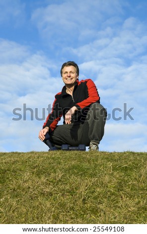 A handsome forties man wearing a tracksuit is crouching down on the grass with his dumbells next to him.
