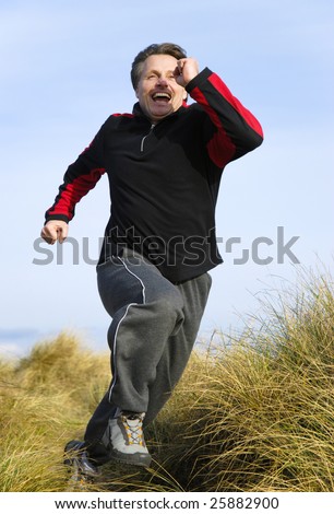A fit fit forties man is laughing as he runs at speed through san dunes,