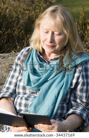 A beautiful older lady is sitting down and reading a book.
