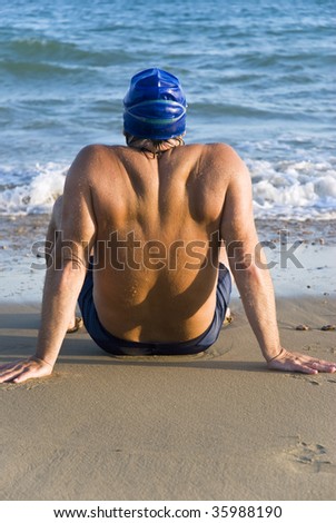 Color portrait of the back view of a muscular male swimmer on beach.