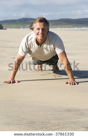 A colour photo of a happy smiling forties man performing exercises on a beautiful big sandy beach.