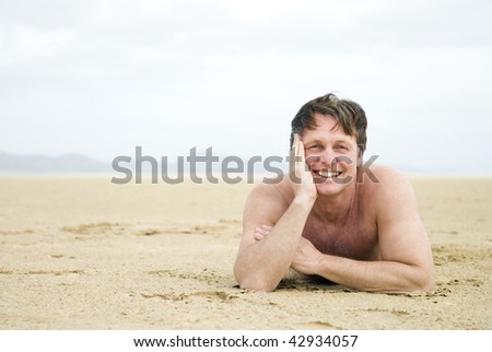 A colour landscape photo of a happy smiling forties man laying alone on a large empty beach