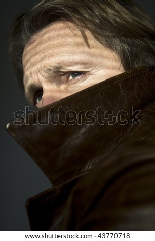 A colour portrait photo of a man peering over the top the collar of his leather coat