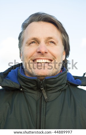 A colour portrait photo of a happy smiling mature man with stubble wearing a winter coat.