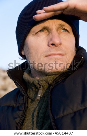 A colour portrait photo of an outdoor man wearing a bodywarmer and hat with stubble on his face