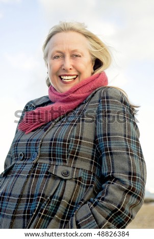 A colour portrait photo of a beautiful older woman in her sixties looking towards the viewer and smiling.