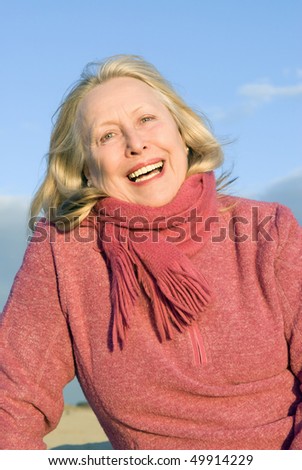 A colour portrait photo of a beautiful older woman in her sixties smiling towards the camera.