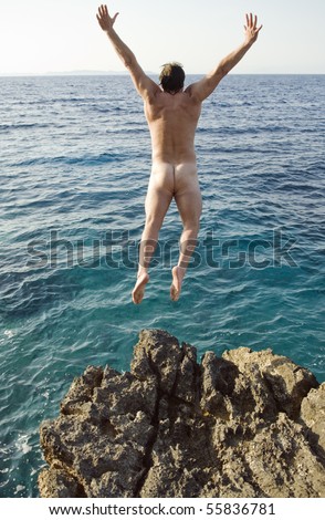 A color photo of a naked man jumping into the sea with his arms outstretched.